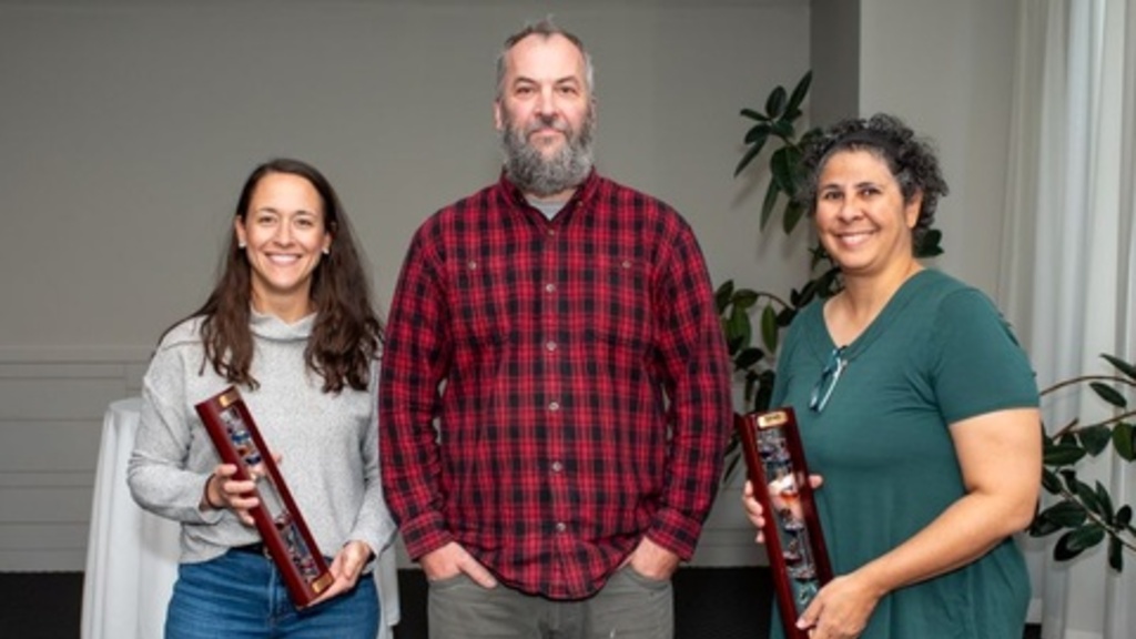 3 award recipients stand in a line and smile, holding their 10-year awards