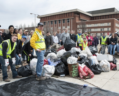 A big group of people poses with an impressive pile of trash.