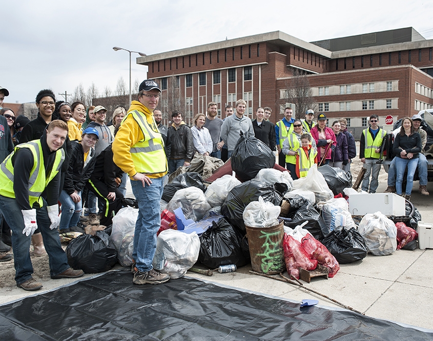 A big group of people poses with an impressive pile of trash.