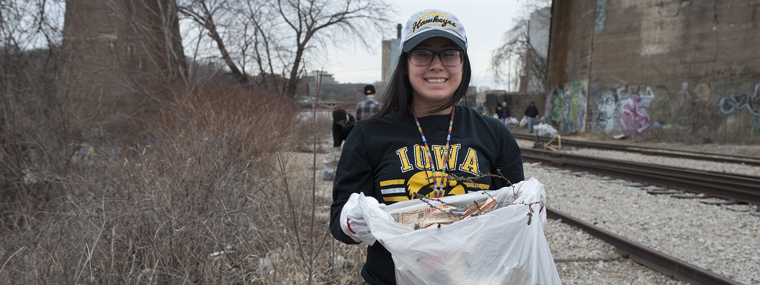 A young woman student picks up trash along railroad tracks