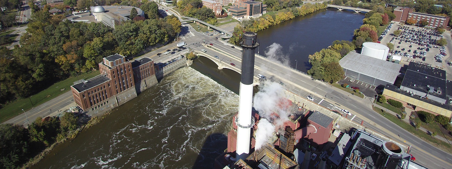 Aerial view of a five story, red brick builting near a river and a dam.
